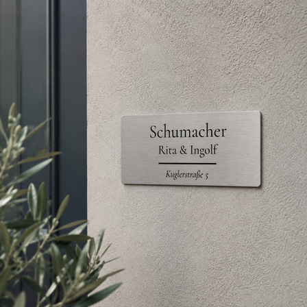 Bedrucktes Edelstahlschild mit der Aufschrift „Schumacher – Rita & Ingolf – Kuglerstraße 5“, an einer hellen Hausfassade neben dem Eingangsbereich angebracht.