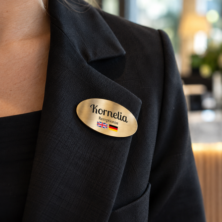 Brushed brass name badge pinned to a receptionist's black blazer at a hotel reception