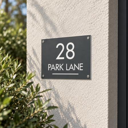 Grey engraved plastic house number sign reading 28 Park Lane screwed to a rendered house facade