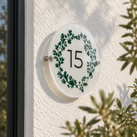 Round acrylic house sign with a green wreath and the number 15 mounted with stainless steel standoffs on a rendered house wall
