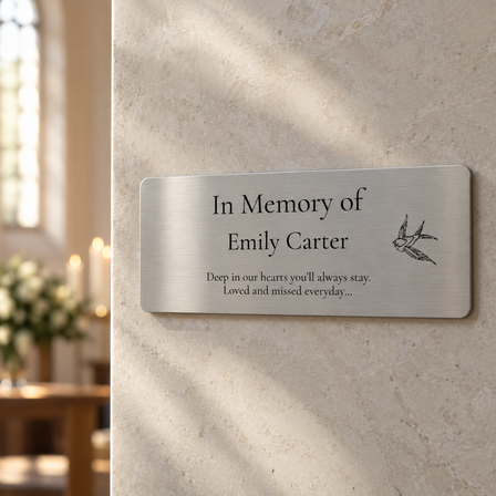 Brushed stainless steel memorial plaque mounted on a smooth stone wall in a chapel