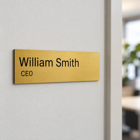 Gold engraved plastic name plate with black text on an office wall next to a door