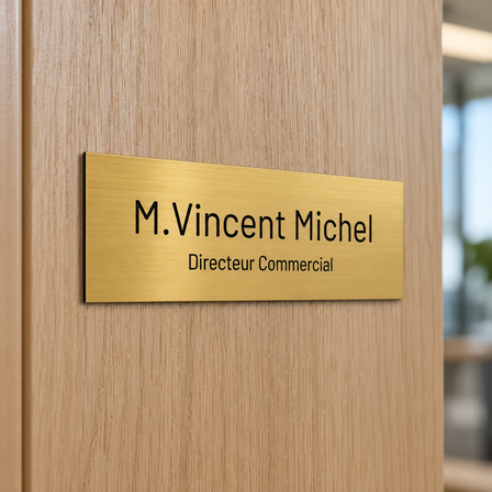 Plaque de porte gravée dorée avec nom et fonction, collée sur une porte de bureau en bois